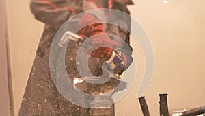 Portrait of man in boilersuit and gloves in enterprise cuts a metal part with angle grinder.