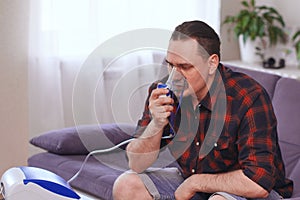 Portrait of a man breathing through an inhaler mask at home.Treatment of pulmonary diseases. copy space