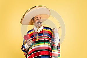 Portrait of man in bright garment and sombrero isolated over yellow background