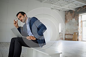 Portrait of man, businessman, worker sitting with laptop with thoughtful expression in big empty room. Opening new