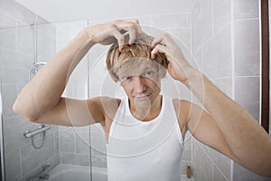 Portrait of man checking for white hair in bathroom