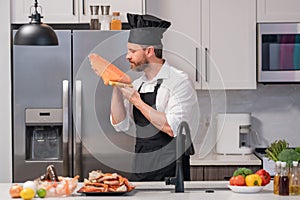 Portrait of man in chef apron and cook hat preparing fresh natural meal salmon at kitchen. Handsome cheerful chef man