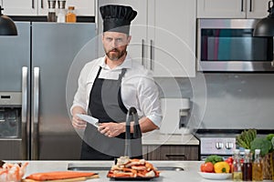 Portrait of man in chef apron and cook hat preparing fresh natural meal salmon at kitchen. Handsome cheerful chef man