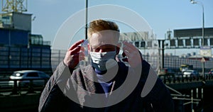 Portrait of a man on a city street. he puts a disposable mask on his face and adjusts it