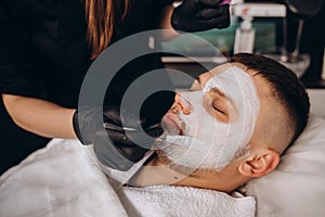 Portrait of man with clay facial mask in beauty spa.