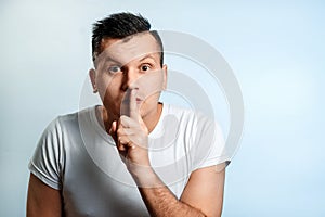 Portrait of a man close-up. Shows a hand gesture quietly, do not make noise, gesture a finger to the lips. On a light background.