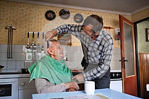 Portrait of man combing hair of elderly father indoors at home.