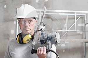 Portrait of man construction worker with jackhammer with safety hard hat, hearing protection headphones and protective glasses.