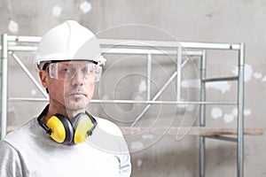 Portrait of man construction worker with safety hard hat, hearing protection headphones and protective glasses. look at the camera