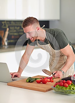 Portrait of man cooking vegetable in the kitchen while looking at a laptop computer on the table