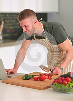 Portrait of man cooking vegetable in the kitchen while looking at a laptop computer on the table