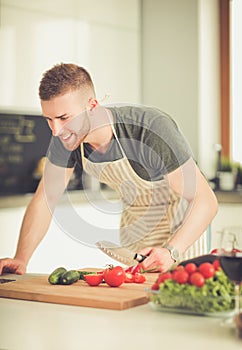 Portrait of man cooking vegetable in the kitchen while looking at a laptop computer on the table