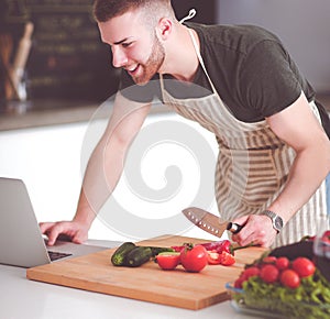 Portrait of man cooking vegetable in the kitchen while looking at a laptop computer on the table