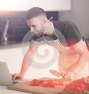 Portrait of man cooking vegetable in the kitchen while looking at a laptop computer on the table