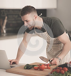 Portrait of man cooking vegetable in the kitchen while looking at a laptop computer on the table