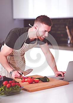 Portrait of man cooking vegetable in the kitchen while looking at a laptop computer on the table