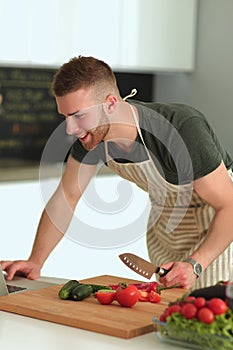 Portrait of man cooking vegetable in the kitchen while looking at a laptop computer on the table