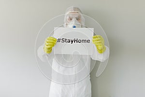 Portrait of man doctor in protective clothes during coronavirus pandemic. holding an inscription stayhome