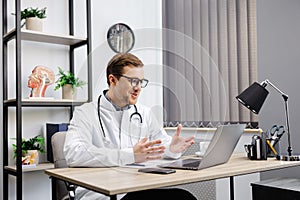 Portrait of man doctor talking to online patient on laptop screen sitting at clinic office desk giving online consultation for