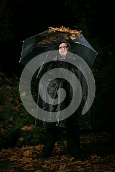 Portrait of a man dressed as Dracula. The guy holds an open umbrella in his hands. The umbrella glows in the night