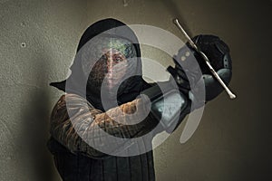 Portrait of a man dressed in black historical fencing armor and fencing protective helmet mask with a long medieval sharp sword