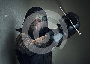 Portrait of a man dressed in black historical fencing armor and fencing protective helmet mask with a long medieval sharp sword