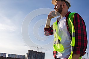 A portrait of man engineer with smartphone in a construction site, working.