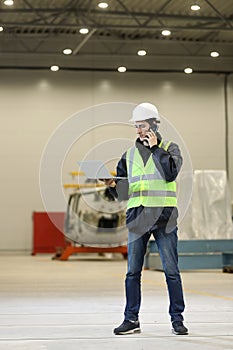 Portrait of a man , factory engineer in work clothes holding laptop and phone, controlling the work process