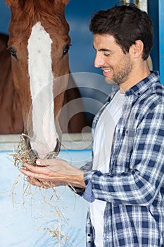 Portrait man farm worker feed horse in stable