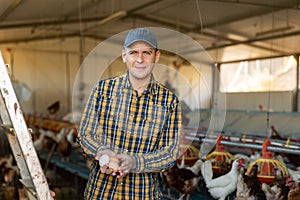 Portrait of man farmer holding eggs in hands in henhouse