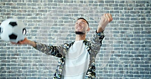 Portrait of man with football celebrating victory on brick wall background