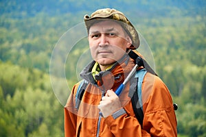 Portrait of a man geologist with a backpack and a geological hammer against the wooded mountain landscape