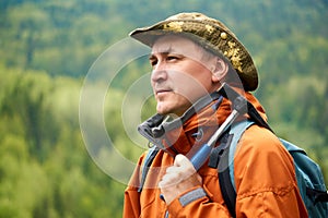 Portrait of a man geologist with a backpack and a geological hammer against the wooded mountain landscape