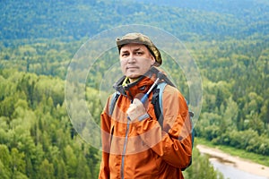 Portrait of a man geologist with a backpack and a geological hammer against the wooded mountain landscape