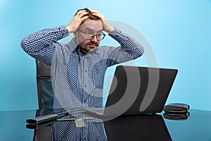 Portrait of man in glasses and checkered shirt, programmer, web developer touching head in despair isolated over blue