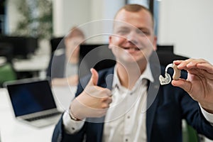 Portrait of a man holding a hearing aid and showing thumbs up in the office.