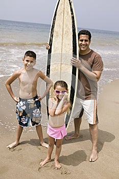 Portrait of man holding surfboard with children on beach
