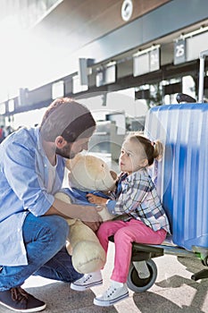 Portrait of man holding teddy bear and playing with his daughter in check in area at airport