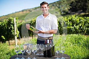 Portrait of man holding wine bottle by table at vineyard