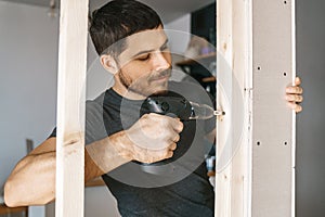 Portrait of a man in home clothes with a screwdriver in his hand fixes a wooden construction for a window in his house. photo