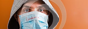 Portrait of a man in hood on his head wearing medical mask with epidemic word at brown background. concept.