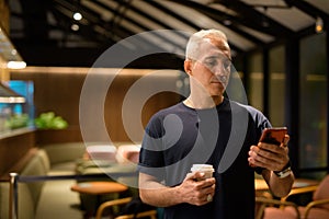 Portrait of man inside coffee shop at night using mobile phone