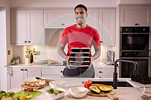 Portrait Of Man In Kitchen Wearing Fitness Clothing Making Batch Of Healthy Meals For Freezer