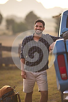 Portrait Of Man Loading Backpack Into Pick Up Truck For Road Trip To Cabin In Countryside