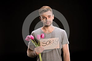 Portrait of man looking to camera while holding tulips bouquet and sorry sign