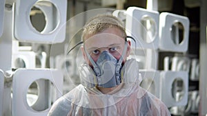 Portrait of a man in a mask in the paint shop. He is wearing a protective mask and a protective robe, he looks at the
