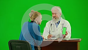 Portrait of man medic on chroma key green screen. Close up senior doctor sitting at table with woman patient showing