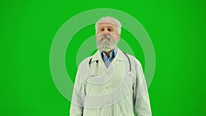 Portrait of man medic on chroma key green screen. Close up senior doctor in white coat talking at the camera, giving