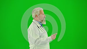 Portrait of man medic on chroma key green screen. Close up senior doctor in white coat talking at the camera, giving