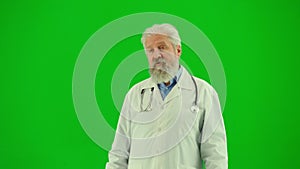 Portrait of man medic on chroma key green screen. Close up senior doctor in white coat talking showing at empty area for